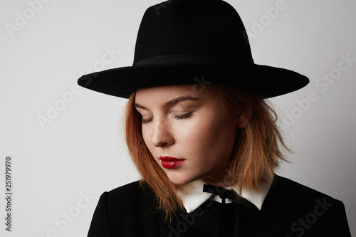 Close up fashion portrait of trendy woman in stylish clothes and black hat posing on white background