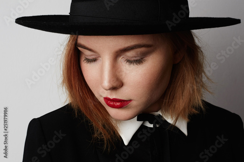 Close up fashion portrait of trendy woman in stylish clothes and black hat posing on white background