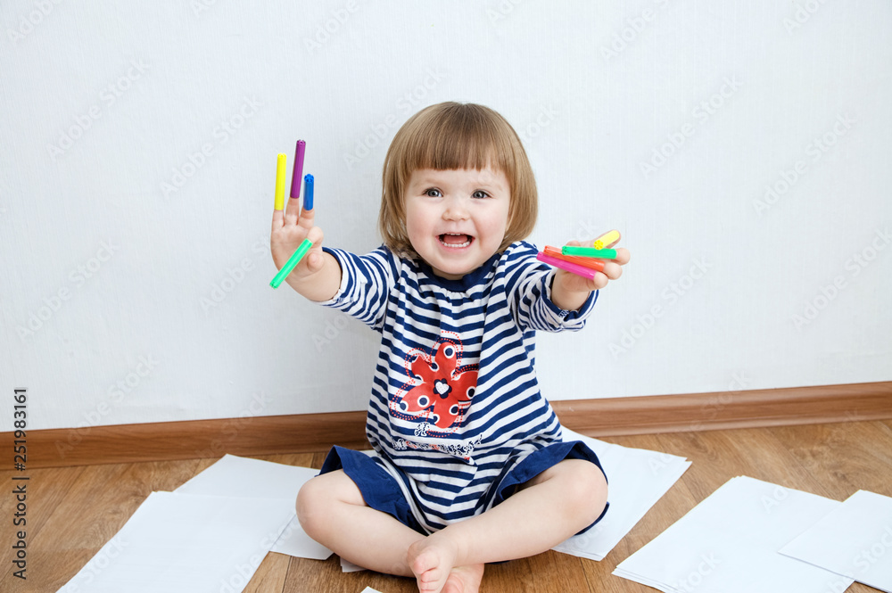child happy smiling sitting on floor playing with felt tip pens. baby girl painting and playing. colorful stuff felt pen caps on fingers of kid child happy smiling sitting on floor playing with felt tip pens. baby girl painting and playing. colorful stuff felt pen caps on fingers of kid
