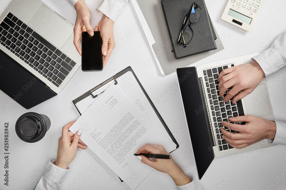 top view of businesspeople typing on laptop, holding smartphone and signing document top view of businesspeople typing on laptop, holding smartphone and signing document