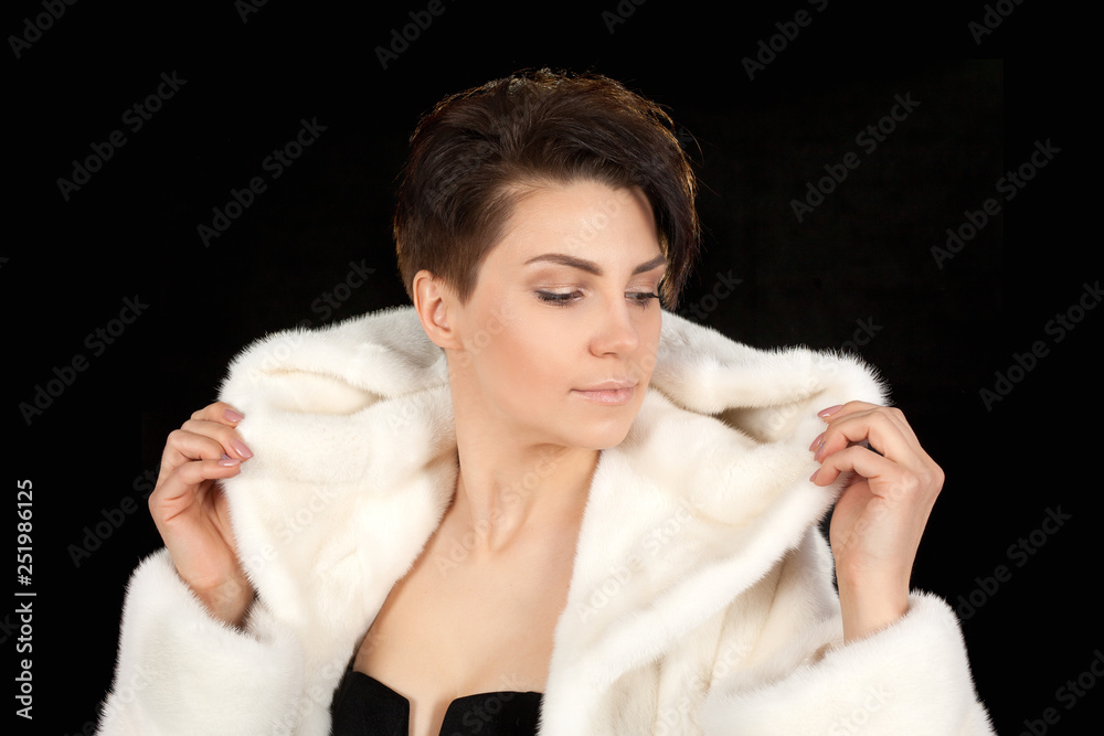 The young beautiful woman in a white fur coat on a black background looking away. The young beautiful woman in a white fur coat on a black background looking away.