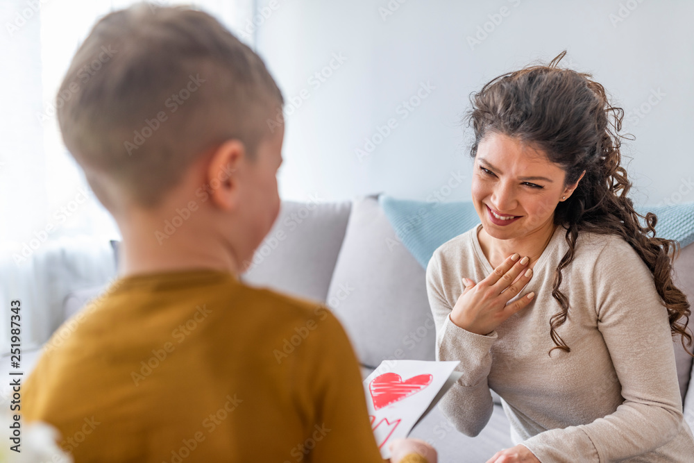 Attractive young woman with little cute boy are spending time together at home while sitting on bed. Happy family concept. Mother's day.