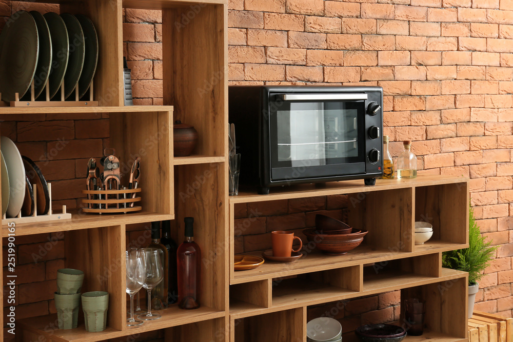 Set of clean dishes with utensils and microwave oven on wooden shelves near brick wall Set of clean dishes with utensils and microwave oven on wooden shelves near brick wall