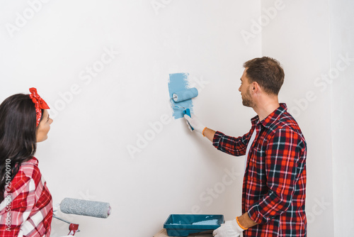  man painting wall in blue color near woman holding roller