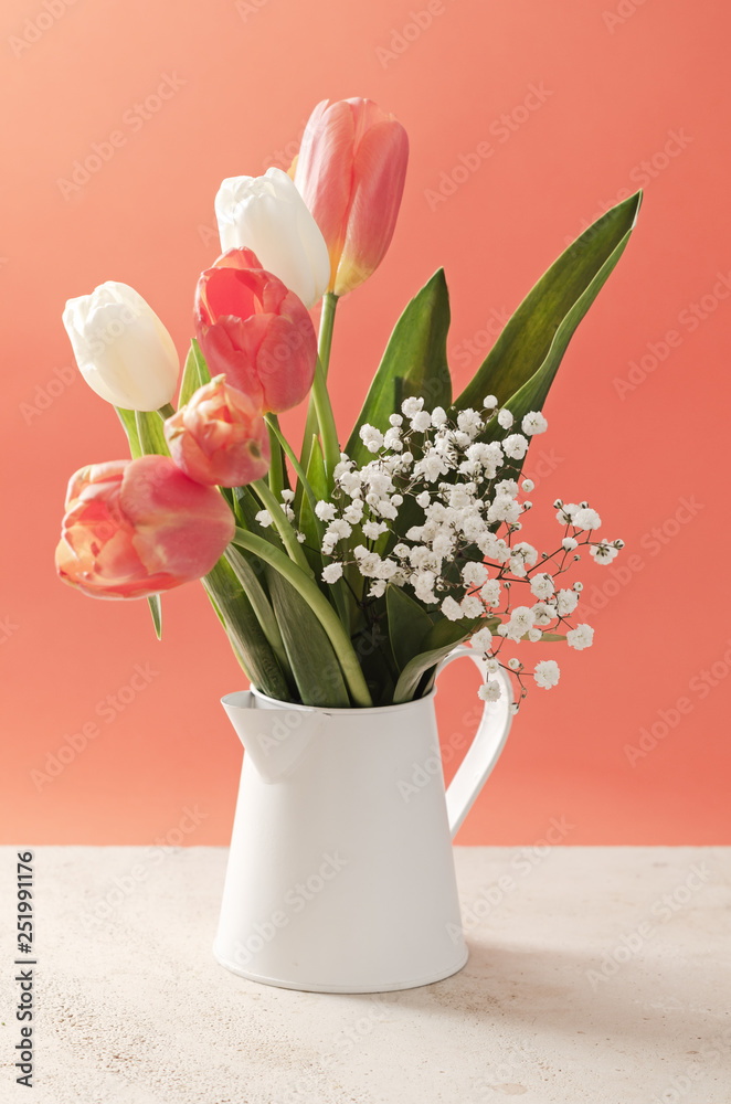 Tulip flowers in a vase on marble table and coral background with  space for text.