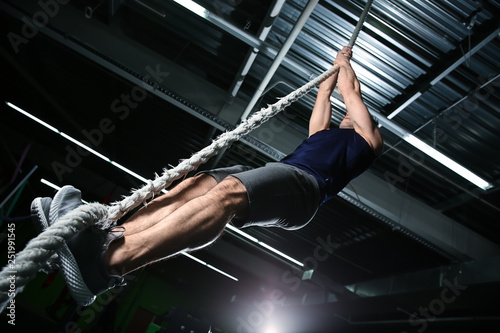 Young sporty man climbing up the rope in gym