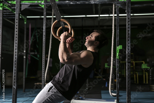 Young sporty man training with gymnastics rings in gym