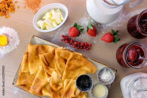 Russian traditional pancakes, blini served with jams, sour cream, and strawberry on the plate. Close-up top view. photo