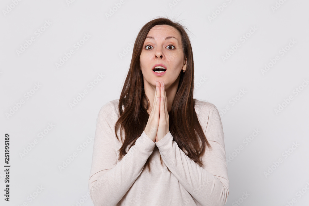 Amazed young woman in light clothes keeping mouth open, holding hands together, praying isolated on white wall background in studio. People sincere emotions, lifestyle concept. Mock up copy space. Amazed young woman in light clothes keeping mouth open, holding hands together, praying isolated on white wall background in studio. People sincere emotions, lifestyle concept. Mock up copy space.