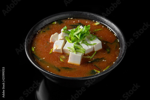 Hot miso soup with seaweed, tofu in bowl on black background. Japanese food.