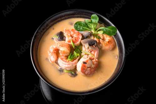 Spicy Thai soup Tom Yam with Coconut milk, Chili pepper and Seafood shrimp and salmon in a plate on a black background. Asian cuisine, restaurant menu.