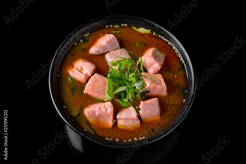 Hot miso soup withsalmon, seaweed, mushrooms, herbs in bowl on black background. Japanese food.