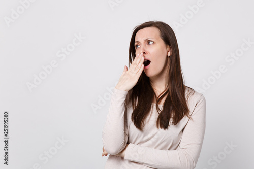 Portrait of tired boring young woman in light clothes looking aside, yawning covering mouth with hand isolated on white wall background. People sincere emotions, lifestyle concept. Mock up copy space.