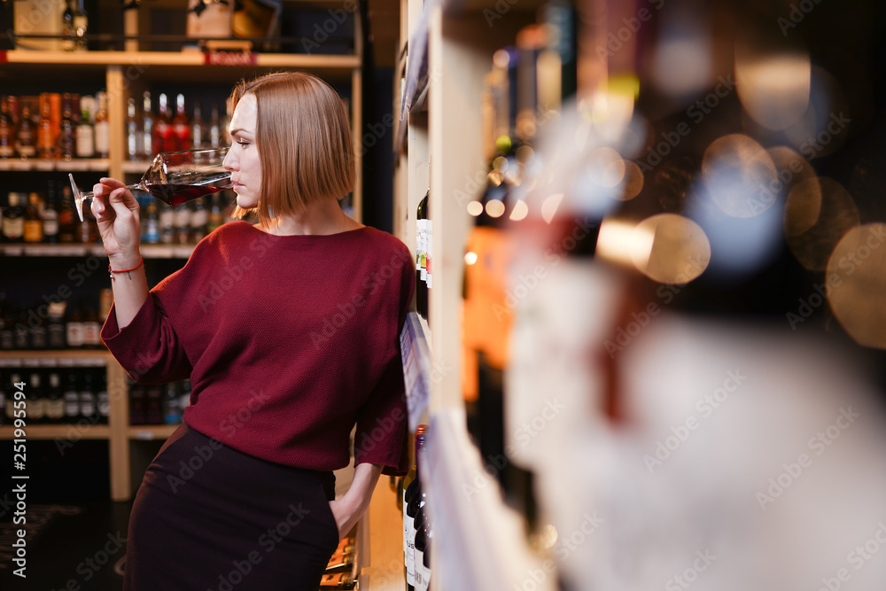 Picture of young woman with wine glass in store on background of shelves