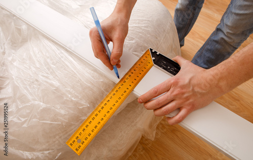 Close up photo of hardworking holding ruler and pencil while making marks on wood at table