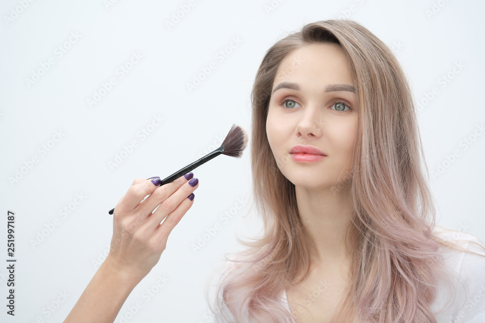 Fototapeta premium Make-up artist makes makeup beautiful blonde girl on a white background. Close-up hands with brush and face.