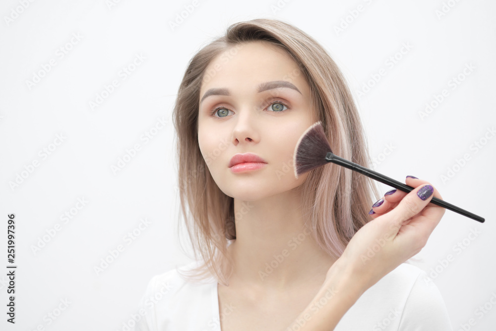 Make-up artist makes makeup beautiful blonde girl on a white background. Close-up hands with brush and face.