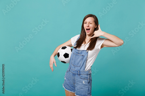 Blinking woman football fan cheer up support favorite team with soccer ball doing phone gesture like says call me isolated on blue turquoise background. People emotions, sport family leisure concept. © ViDi Studio