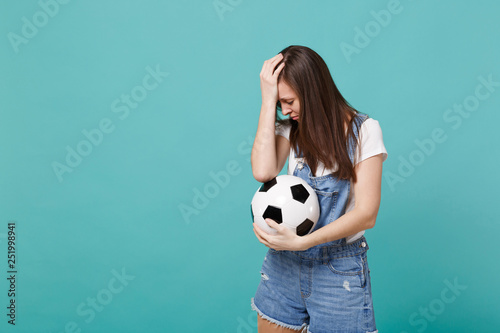 Disappointed woman football fan support favorite team with soccer ball putting hand on lowered head isolated on blue turquoise wall background in studio. People emotions, sport family leisure concept. © ViDi Studio