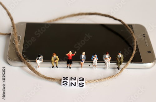A variety of miniature people sitting on Smart phone. 'SNS' alphabetic white cube with rope.