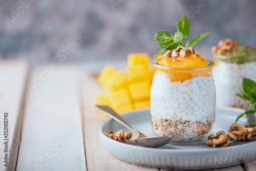 Homemade pudding of Chia seeds and almond milk with cereals and puree of mango and kiwi with walnuts and mint in glass jars. Vegan healthy morning breakfast or superfood dessert
