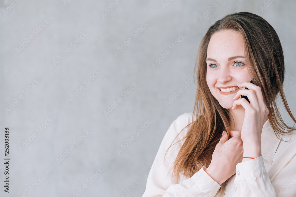 Young woman portrait. Excited beautiful female talking on phone looking at virtual advertisement. Copy space on grey background. Young woman portrait. Excited beautiful female talking on phone looking at virtual advertisement. Copy space on grey background.
