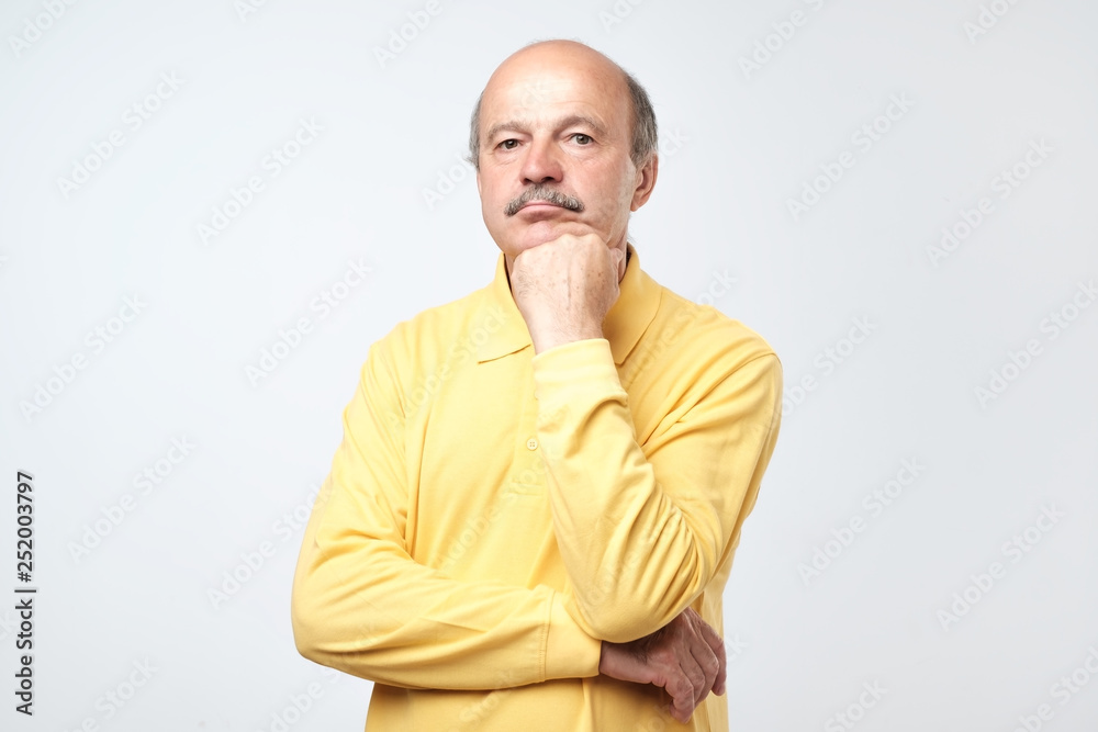 Portrait of casual mature man in yellow shirt thinking and looking puzzled. Portrait of casual mature man in yellow shirt thinking and looking puzzled.