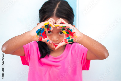 Cute little girl with colorful painted hands on wall background