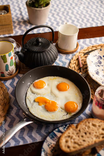 four sunny side up eggs, served in a pan, breakfast table