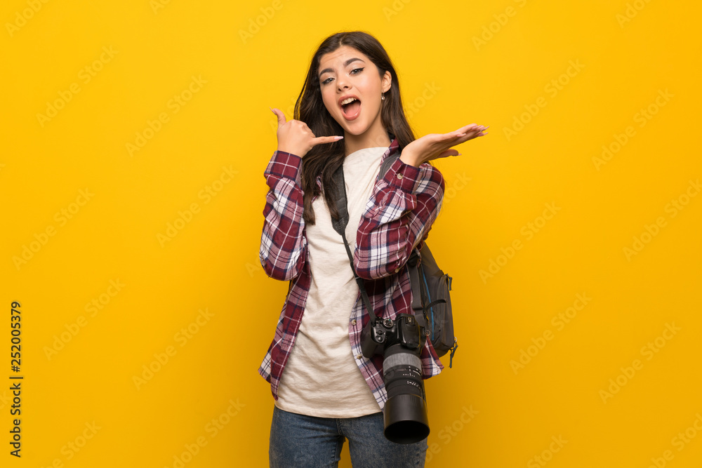 Photographer teenager girl over yellow wall making phone gesture and doubting Photographer teenager girl over yellow wall making phone gesture and doubting