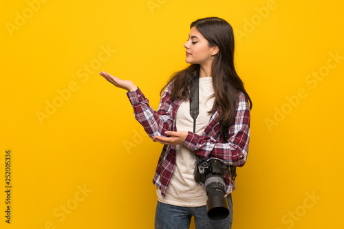Photographer teenager girl over yellow wall extending hands to the side for inviting to come