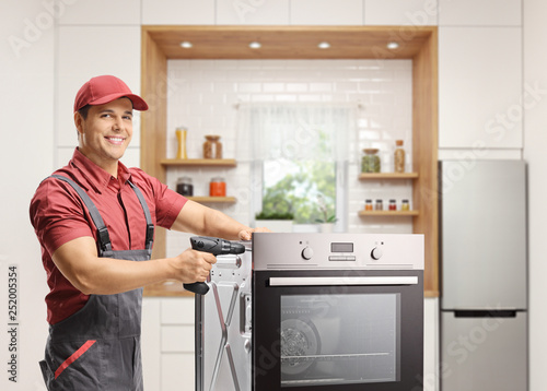 Repairman working with a drill on an oven in a kitchen