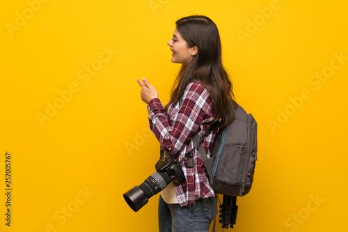Photographer teenager girl over yellow wall pointing back