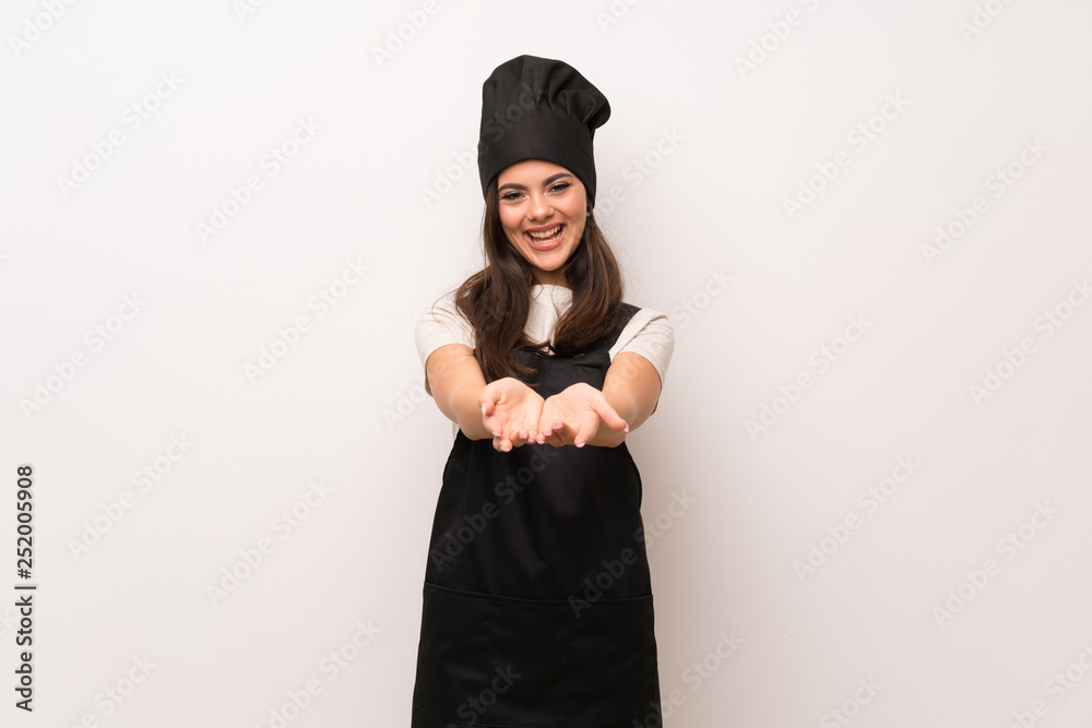Teenager chef over white wall holding copyspace imaginary on the palm to insert an ad Teenager chef over white wall holding copyspace imaginary on the palm to insert an ad