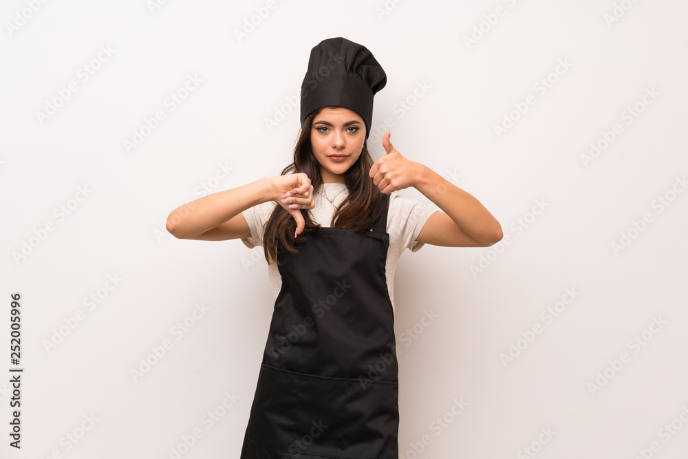 Teenager chef over white wall making good-bad sign. Undecided between yes or not Teenager chef over white wall making good-bad sign. Undecided between yes or not