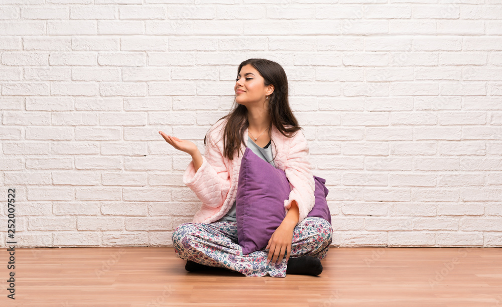 Teenager girl in pajamas holding copyspace imaginary on the palm to insert an ad Teenager girl in pajamas holding copyspace imaginary on the palm to insert an ad