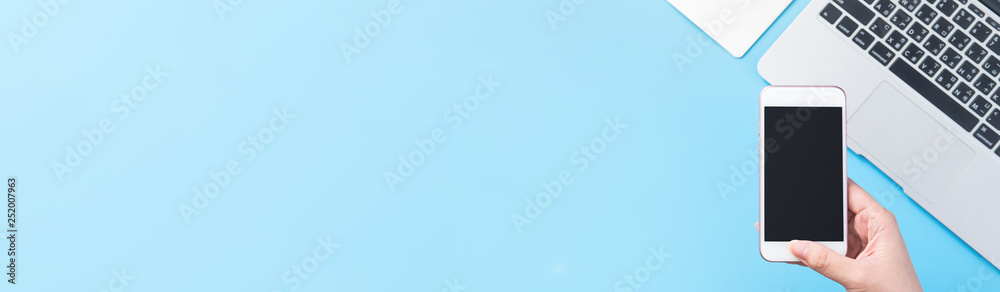 A woman is holding a smartphone isolated with a minimal blue desk, concept of online shopping payment, internet work at home, e-commerce, copy space, flat lay, top view, mock up A woman is holding a smartphone isolated with a minimal blue desk, concept of online shopping payment, internet work at home, e-commerce, copy space, flat lay, top view, mock up