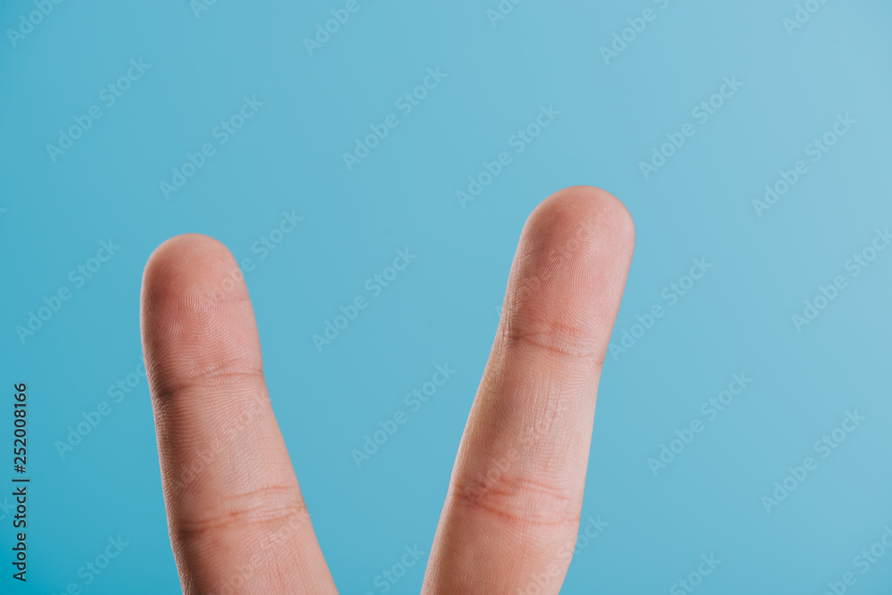 cropped view of fingers with victory sign isolated on blue cropped view of fingers with victory sign isolated on blue