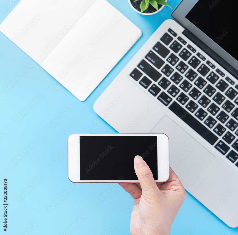A woman is holding a smartphone isolated with a minimal blue desk, concept of online shopping payment, internet work at home, e-commerce, copy space, flat lay, top view, mock up A woman is holding a smartphone isolated with a minimal blue desk, concept of online shopping payment, internet work at home, e-commerce, copy space, flat lay, top view, mock up