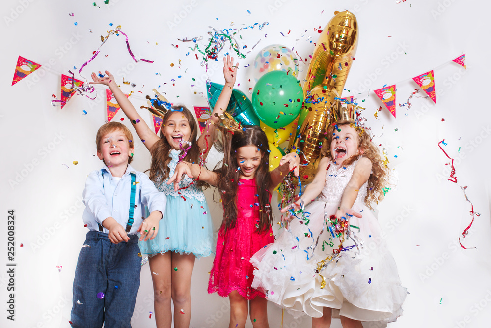 Group of beautiful kids throwing colorful confetti and looking happy on birthday party - obrazy, fototapety, plakaty 