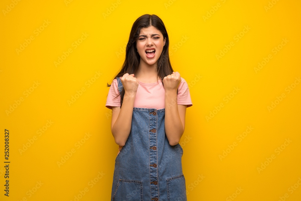 Teenager girl over yellow wall frustrated by a bad situation Teenager girl over yellow wall frustrated by a bad situation