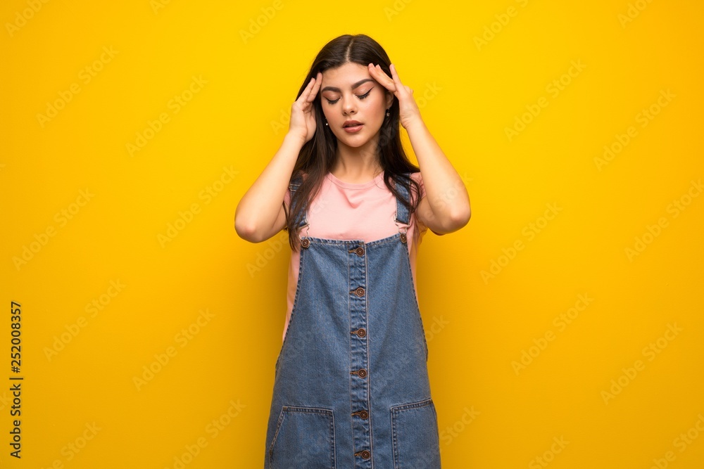 Teenager girl over yellow wall with headache Teenager girl over yellow wall with headache