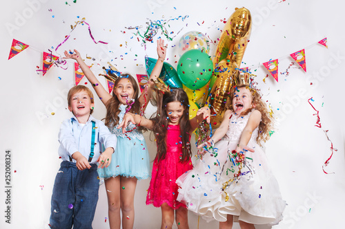 Group of beautiful kids throwing colorful confetti and looking happy on birthday party