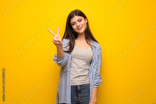 Teenager girl over yellow wall smiling and showing victory sign