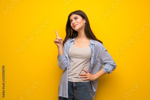 Teenager girl over yellow wall showing and lifting a finger in sign of the best