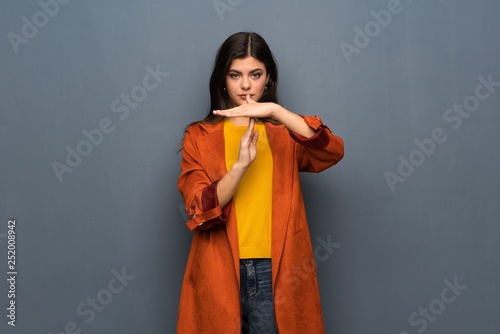Teenager girl with coat over grey wall making time out gesture © luismolinero