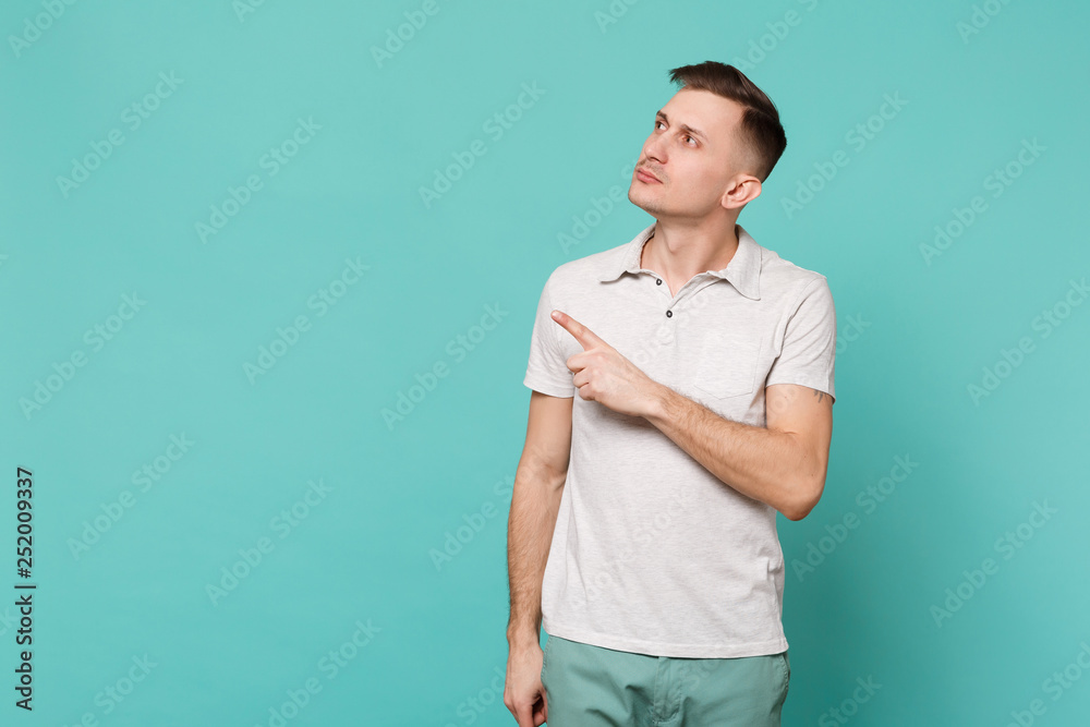 Portrait of handsome young man in casual clothes looking, pointing index finger aside isolated on blue turquoise background in studio. People sincere emotions, lifestyle concept. Mock up copy space. Portrait of handsome young man in casual clothes looking, pointing index finger aside isolated on blue turquoise background in studio. People sincere emotions, lifestyle concept. Mock up copy space.