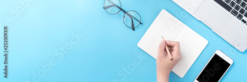 A student write on open white book or accounting isolated on a minimal clean blue workplace at home with smartphone and accessories, copy space, flat lay, top view, mock up photo