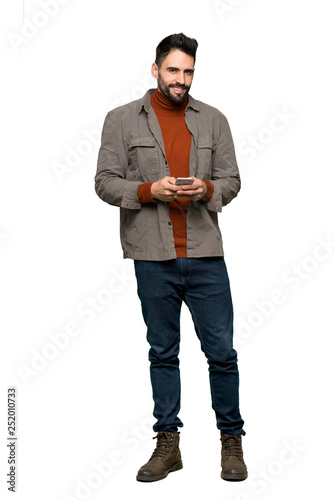 Full-length shot of Handsome man with beard sending a message with the mobile on isolated white background