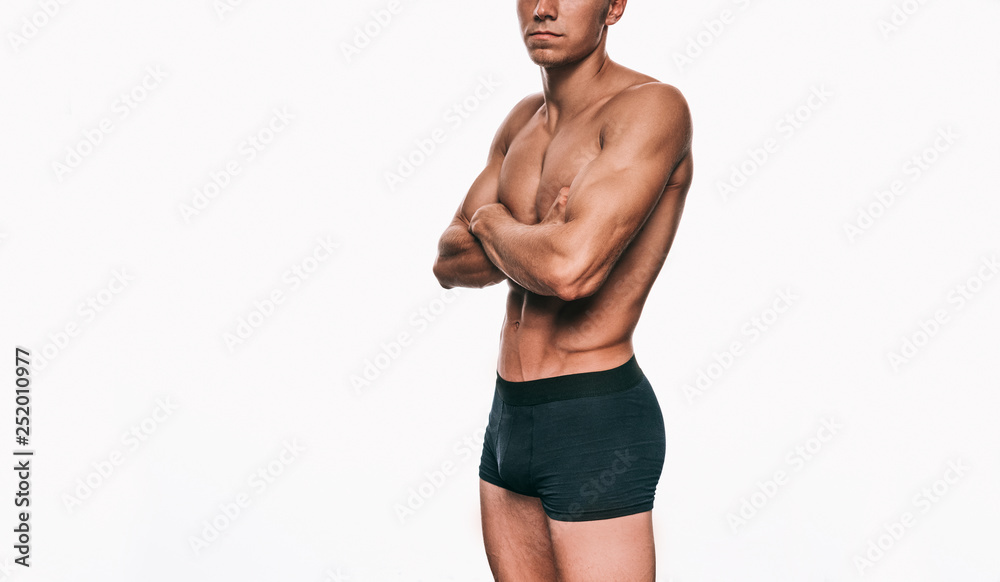 Image of fitness male model in black underwear showing his sexy body isolated on a white background. Shirtless man with sexy abdomen cross hands posing over white wall. Health, sport, people concept